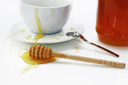 Honey, a wooden dipper and a white cup; illustrative photography.