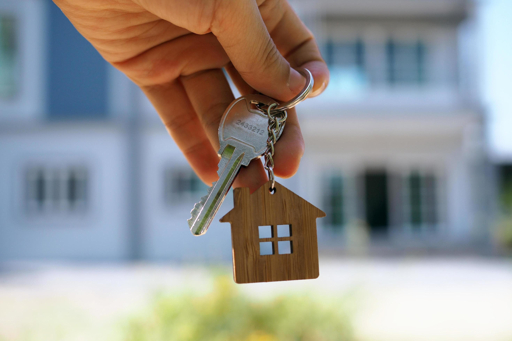 Close-up of a hand holding house keys with a new home in the background, representing first-time homebuyers