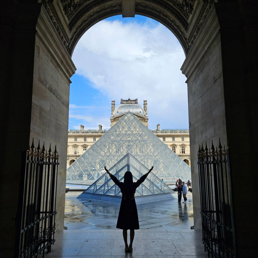 Person with outstretched arms in an archway facing the Louvre Museum, one of the world's major museums, in Paris.