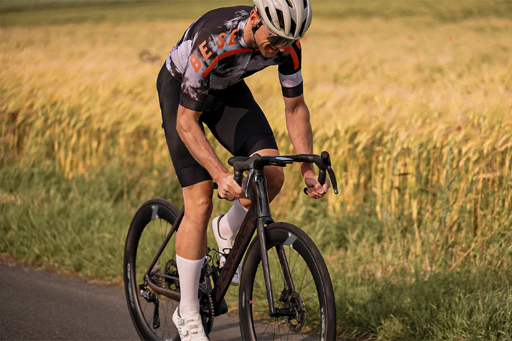 Road cyclist riding a bicycle with deep-section carbon wheels through open countryside.