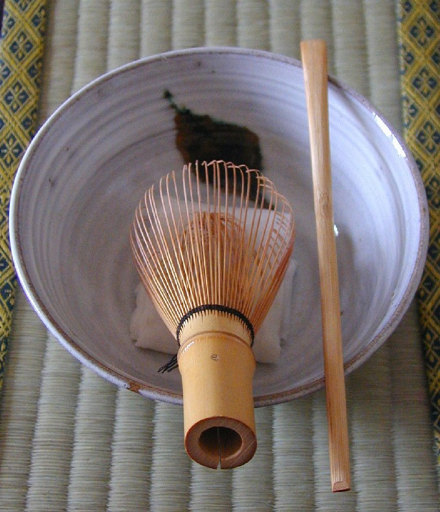 Bamboo chasen whisk resting in a white matcha bowl with green tea powder