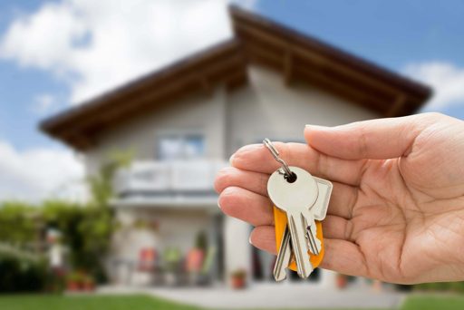 Hand holding house keys in front of a home