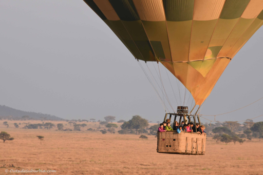 Hot air balloon with passengers floating over the Serengeti at sunrise