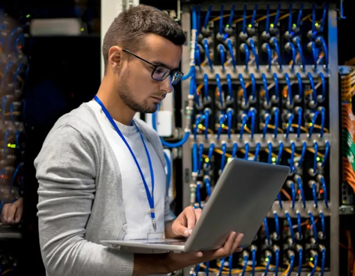 IT support technician holding a laptop in front of a server rack