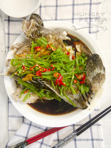 Whole steamed garoupa fish garnished with spring onion and ginger, a Cantonese seafood classic