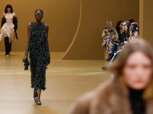 Model wearing fringed black dress walking runway at fashion show